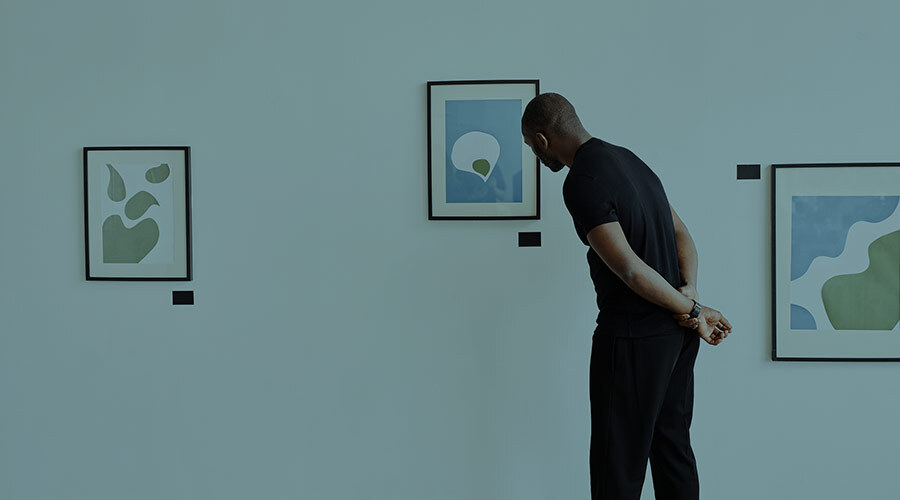 A single young Black man, seen from behind, observes a wall of framed abstract art in a gallery or museum.