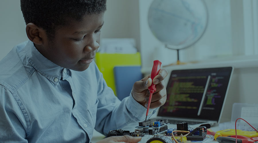 A Black boy uses a soldering iron on a computer circuit board