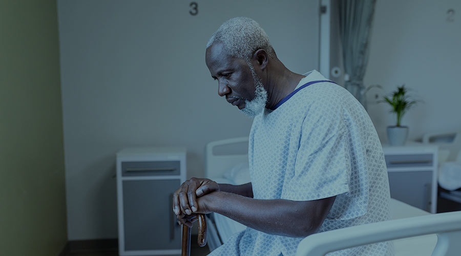 An African American man in a hospital gown sits on a hospital bed