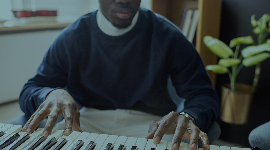 The image shows a young African American student's torso and hands. He is playing a piano in what appears to be a classroom