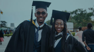 Two smiling Black college graduates stand together wearing caps and gowns