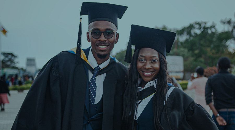 Two smiling Black college graduates stand together wearing caps and gowns