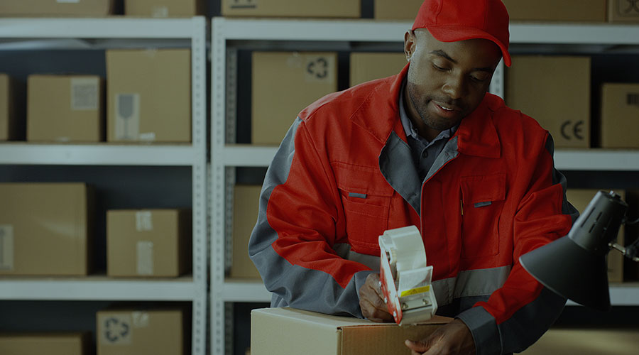 A young Black man in a uniform works with packages in a warehouse.