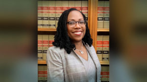 Judge Ketanji Brown Jackson wears a cream colored suit jacket and shirt while standing in a legal library