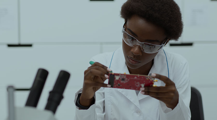A young black engineer wears protective glasses and a white shirt in a lab while working on a small circuit board