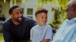 Three Black males representing three generations, a grandfather, a father and his son, sit together at home