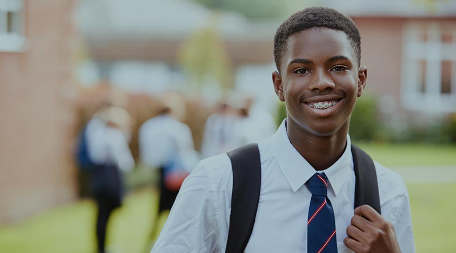 A young Black high school student in a white shirt and tie smiles directly into the camera