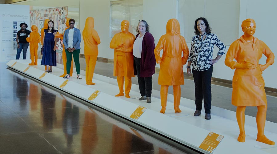 Women scientists stand next to life-sized orange status of themselves at the Smithsonian