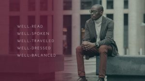 An African American man wearing a blazer and turtleneck sits while holding a cup of coffee.