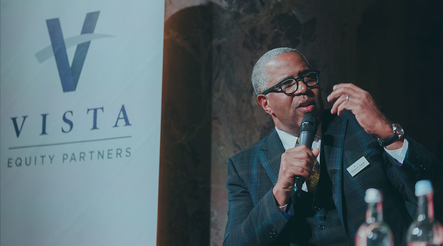 Robert F. Smith of Vista Equity Partners in a plaid suit jacket and glasses holds a microphone for a talk in Berlin