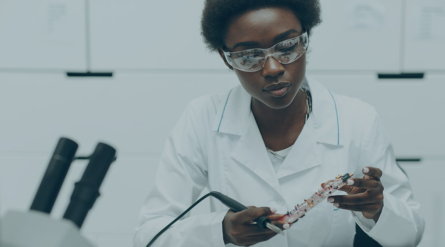 A Black woman scientist carefully examining a lab piece.