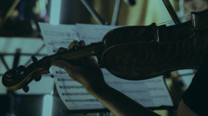 A person holding a violin while looking at sheet music on a stand.