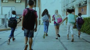 A group of young children wear backpacks as they run to school.