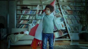 A young Black boy stands in a library and wears a costume rocket ship on his back.