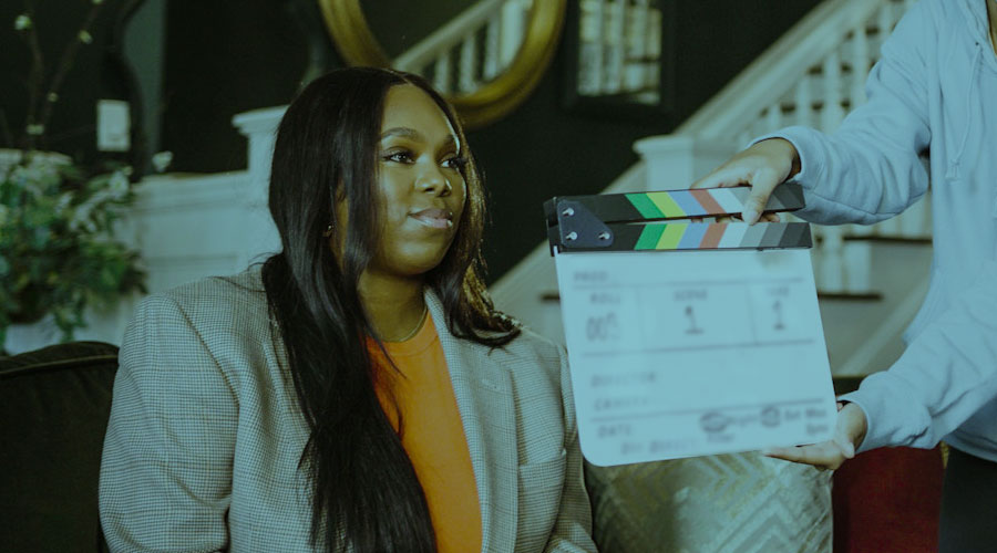 An image of a Black woman while she sits with a clapperboard in front of her.