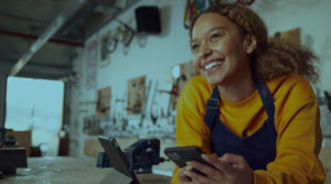 Young female business owner leaning on a counter holding a cellphone.