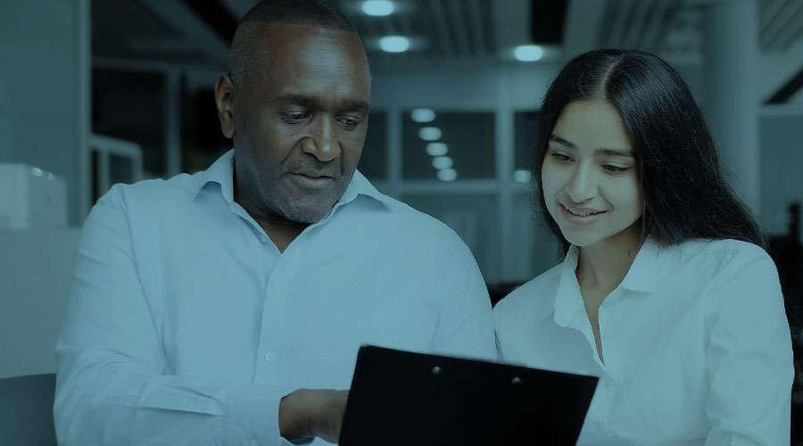 A Black man and Latina women in white button down shirts look together at a clipboard.