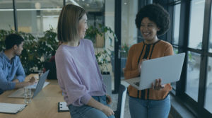 Two women standing in an office setting and smiling at one another