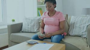 Image of a Black woman in a pink t-shirt going over money and paperwork in a living room setting.