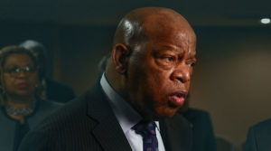 An image of a Black man in a suit giving a speech to a group of people.