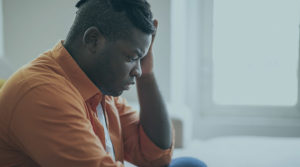 Black American man sitting and wearing an orange button down shirt.