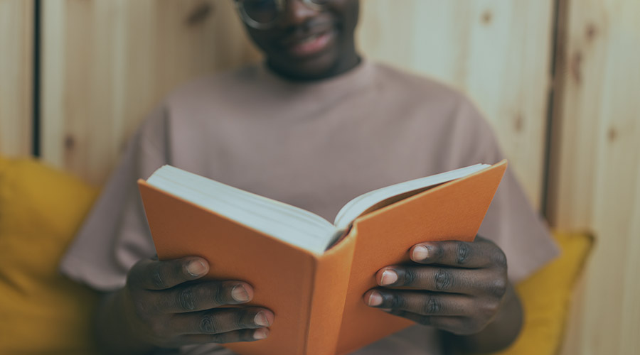 Image of a Black person wearing a tan t-shirt holding an orange book