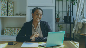 A Black woman sitting at a desk and smiling while looking at her laptop