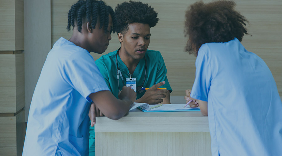 Image of three Black medical professionals who are dressed in scrubs and are standing around a table