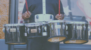 A Black student carrying and playing marching band drums