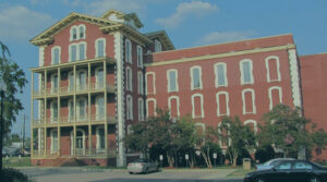 Image of a red brick building with a parking lot and trees in front of it