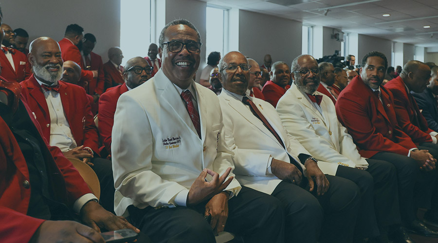 Image of a group of Black men sitting down in white and red suit jackets