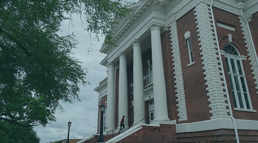 Image of a person walking upstairs into a large brick building with white columns on a school campus