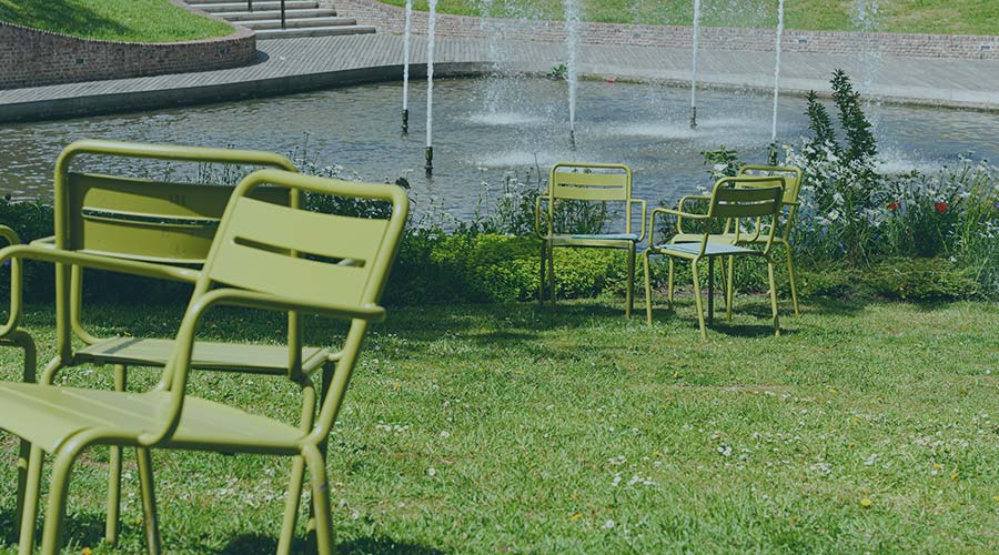 Image of several green chairs on a patch of grass next to a fountain