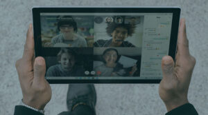 A person holding an iPad with four people in a video call on the screen