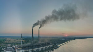 Sun setting over the horizon with smoke stacks releasing fumes