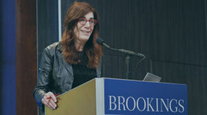 Judy Faulkner in red glasses, black shirt and leather jacket speaking at a podium at an event sponsored by Brookings