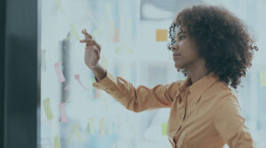 A woman in an orange button-down shirt reaching out for a note on a whiteboard