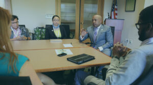 A group of professionally dressed people sitting in a conference room with Daymond John