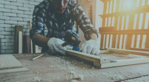 A carpenter wears gloves while working with a hammer on a woodworking project