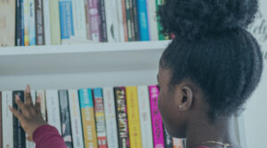 A young woman facing a bookcase and picking one out