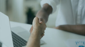 Two people shaking hands over a laptop on a white counter