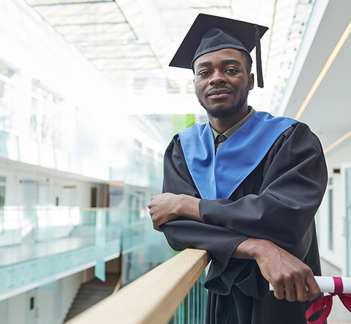 A Black college graduate wears his cap and gown while holding his diploma