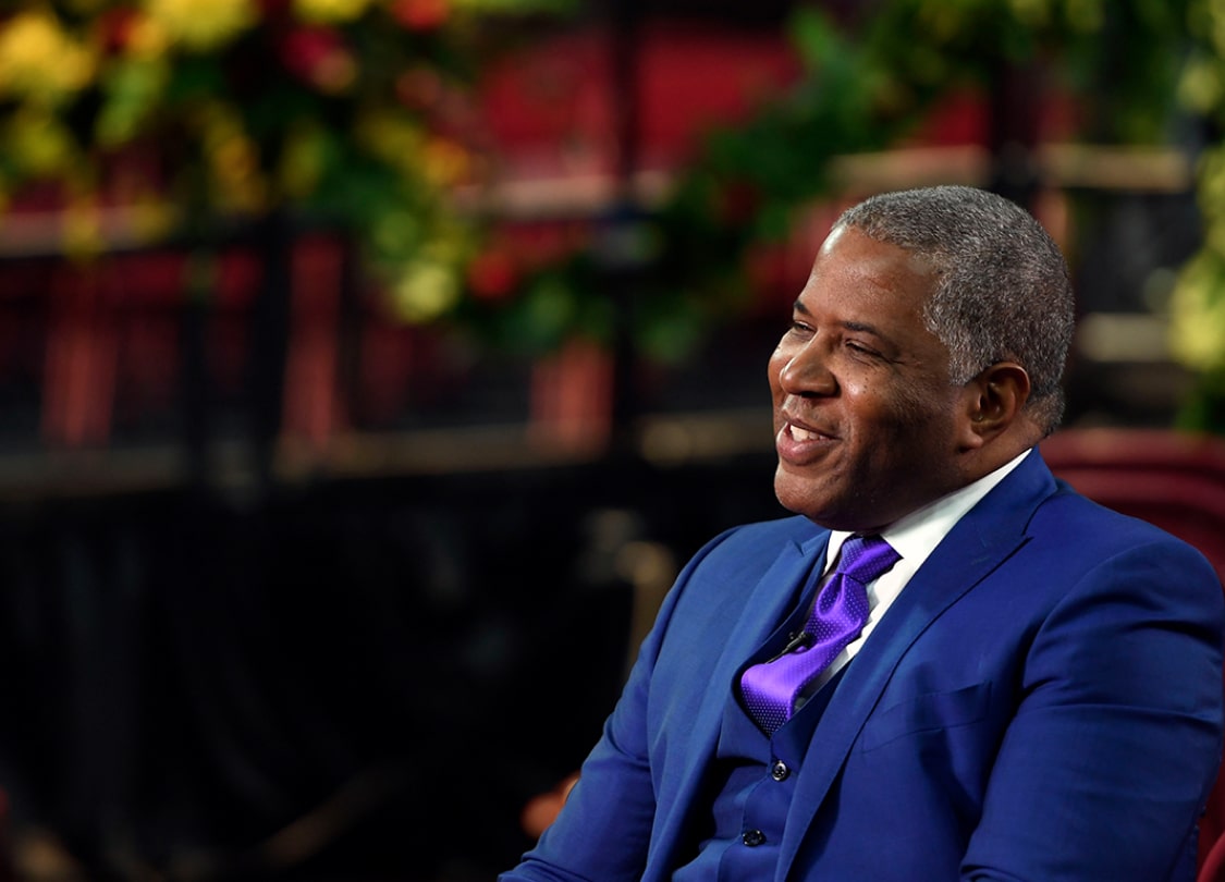 Robert F. Smith wears a blue suit as he sits in a chair smiling
