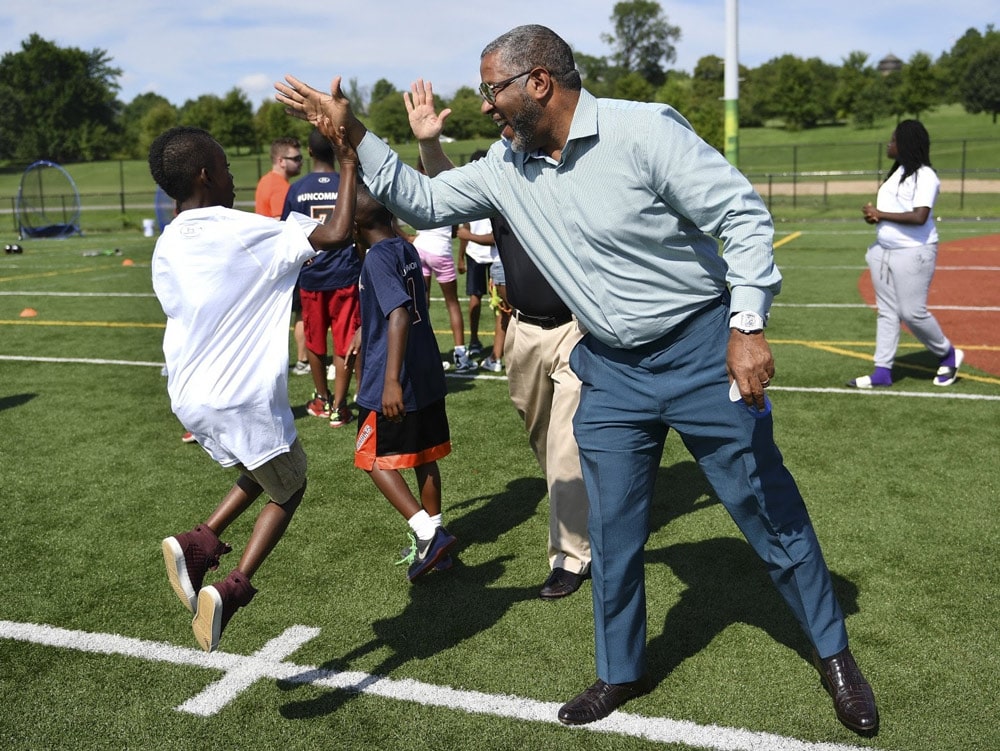 Robert F. Smith pictured outdoors in a suit while he high fives a young child