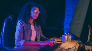 Woman in glasses sitting down at a desk typing on a keyboard and looking at a computer screen