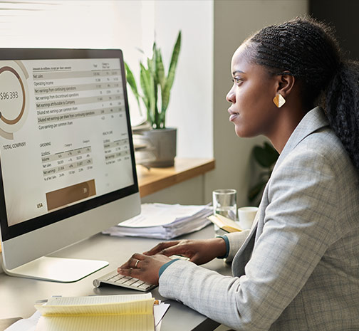 A Black woman sitting at a desk, typing on a keyboard and looking at a computer monitor.