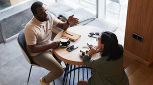 Two people, who may have a mentoring relationship, have a thoughtful conversation while drinking coffee at a small table.