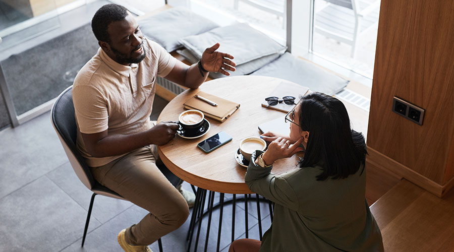 Two people, who may have a mentoring relationship, have a thoughtful conversation while drinking coffee at a small table.