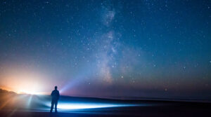 A person shining a light up at the starry night sky.