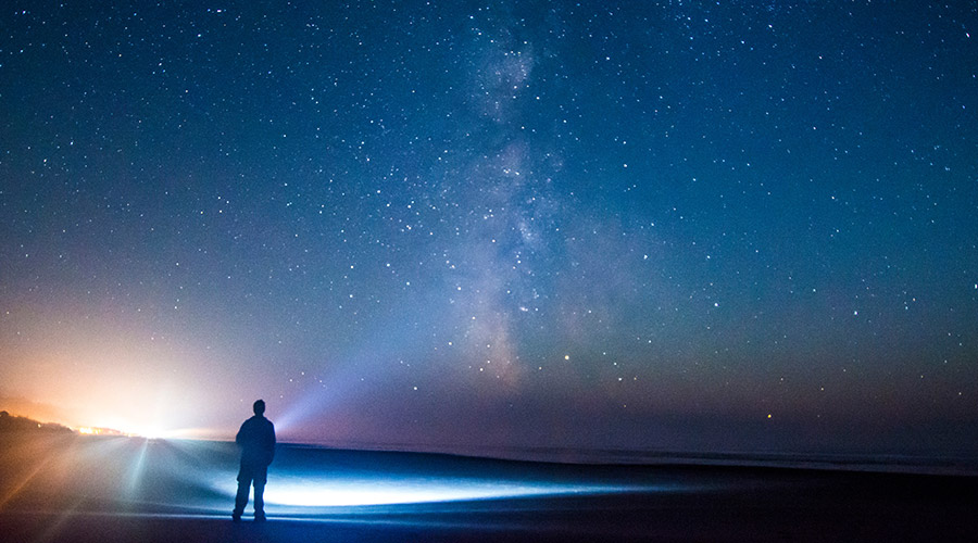 A person shining a light up at the starry night sky.